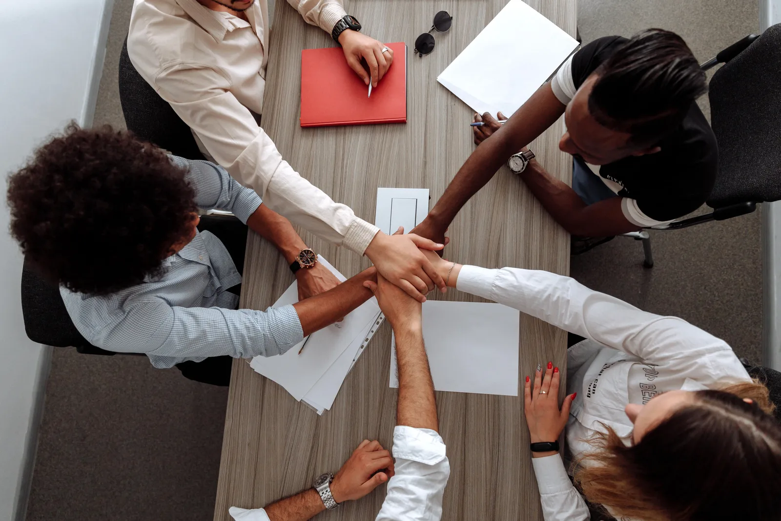 Overhead view of a diverse team placing hands together in a sign of unity during a meeting.