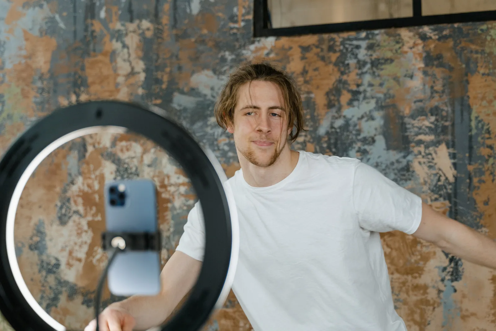 Man filming vlog with smartphone and ring light in an indoor setting. Casual attire.