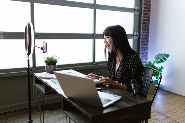 Asian woman in office setting recording content with laptop and ring light, showcasing elegant business setup. Verificare la qualità del pubblico